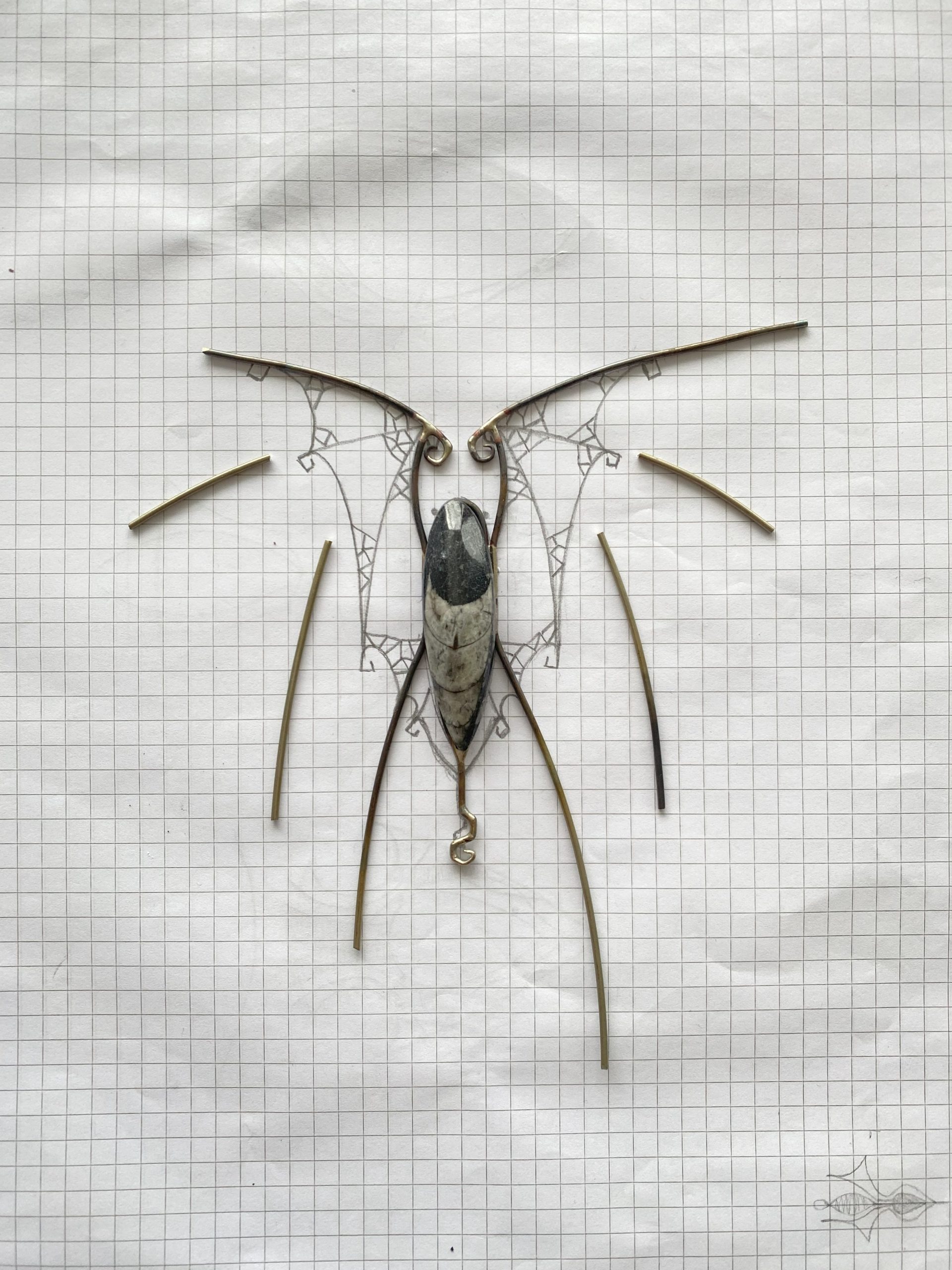 A Vottovara in progress, featuring a central stone placed on a sketched design with wire components arranged for assembly, laid out on graph paper.